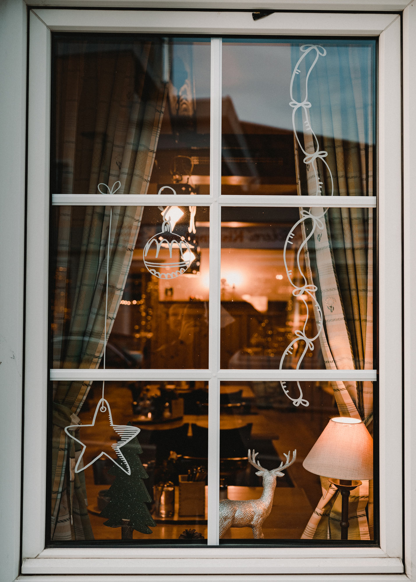 Gasthausfenster mit weißer Bemalung: Ein Stern an einer Schnur, eine Christbaumkugel und viele Würste hängen von oben herab.