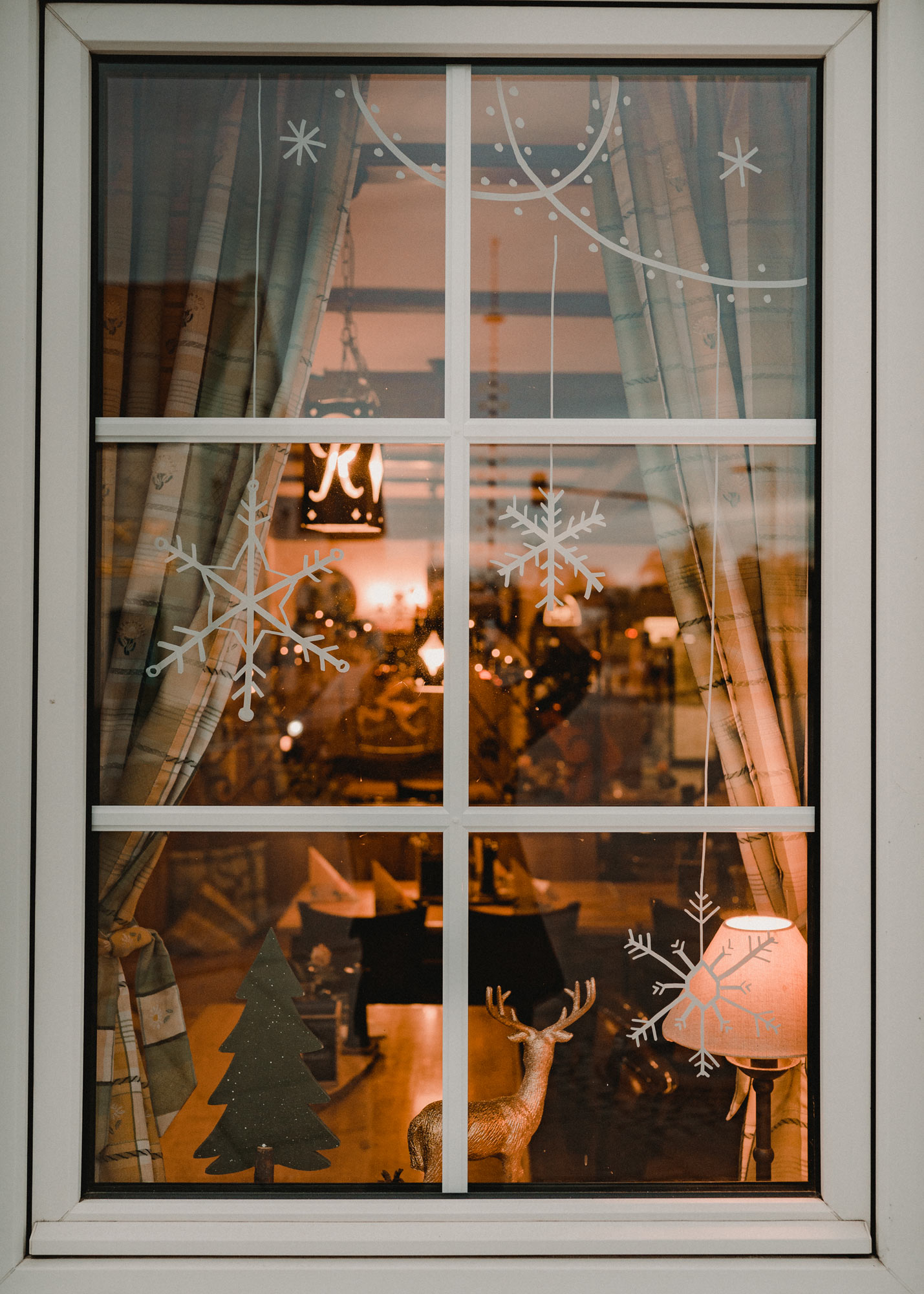 Gasthausfenster mit weißer Bemalung: Lichtergirlanden und Schneeflocken.