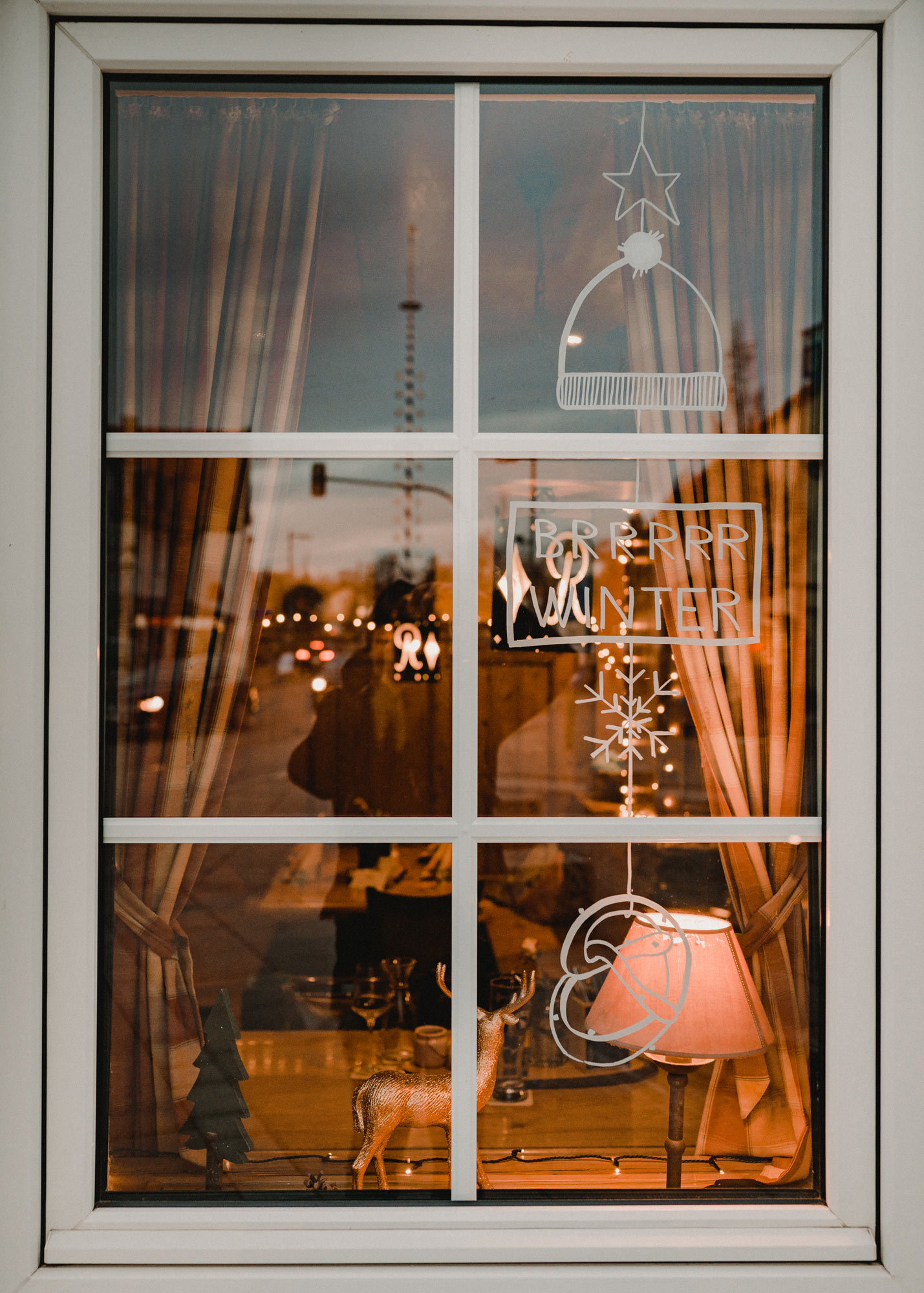 Gasthausfenster mit weißer Bemalung: Ein Mobile bestehend aus einem Stern, Mütze, Schild, Schneeflocke und Breze.